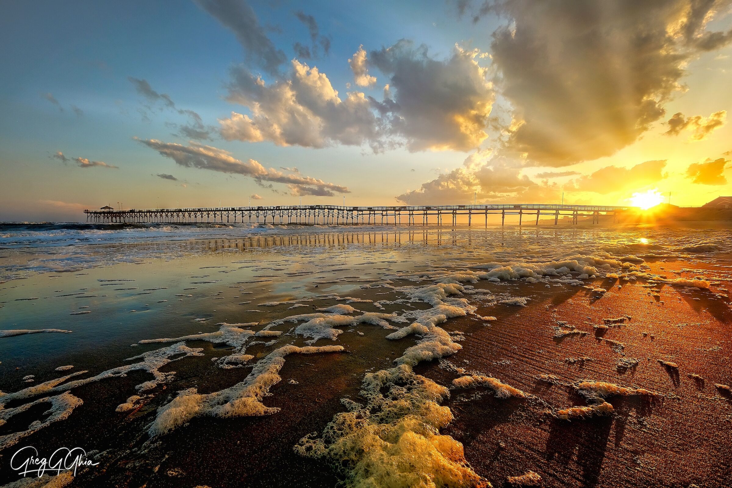 Pier is seen on the beach at sunset with a strikingly golden sky that casts a warm light on the sand and water as the waves roll in.